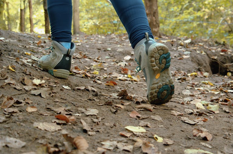 Close-up of a hiker's trekking shoes on a leaf-covered trail in autumn.